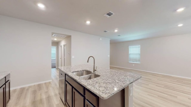 kitchen featuring sink, light stone counters, light wood-type flooring, stainless steel dishwasher, and a kitchen island with sink