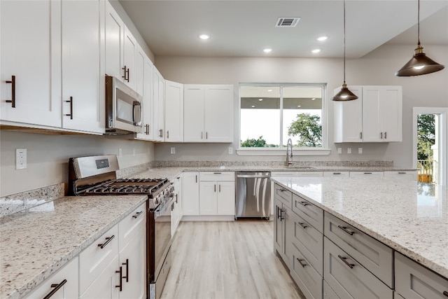 kitchen with appliances with stainless steel finishes, light hardwood / wood-style flooring, white cabinets, decorative light fixtures, and light stone countertops