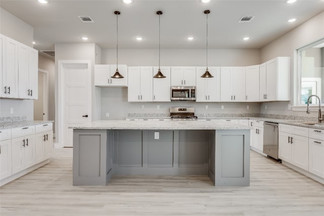 kitchen featuring appliances with stainless steel finishes, light stone counters, pendant lighting, light wood-type flooring, and a large island