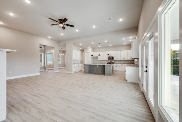 interior space featuring white cabinetry, tasteful backsplash, light wood-type flooring, ceiling fan, and an island with sink