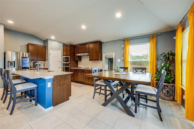 kitchen featuring a kitchen bar, vaulted ceiling, sink, a center island with sink, and light tile patterned flooring