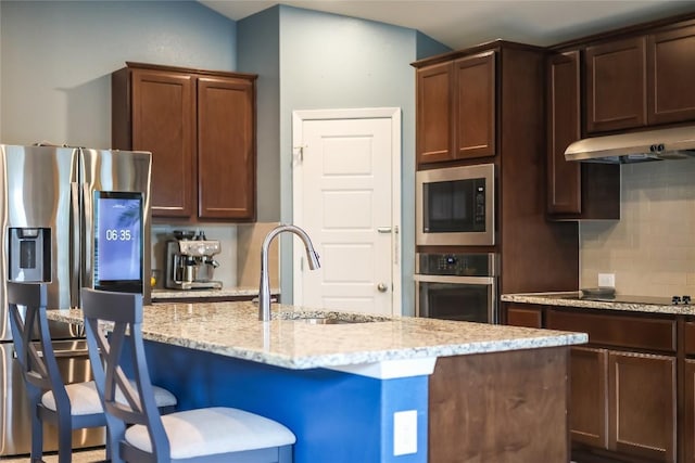 kitchen featuring decorative backsplash, light stone counters, stainless steel appliances, sink, and a center island with sink