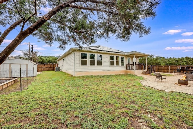 20400 Bear Rd, Lago Vista, TX 78645 - back of house featuring a fenced backyard, roof mounted solar panels, a lawn, central AC unit, and an outdoor fire pit