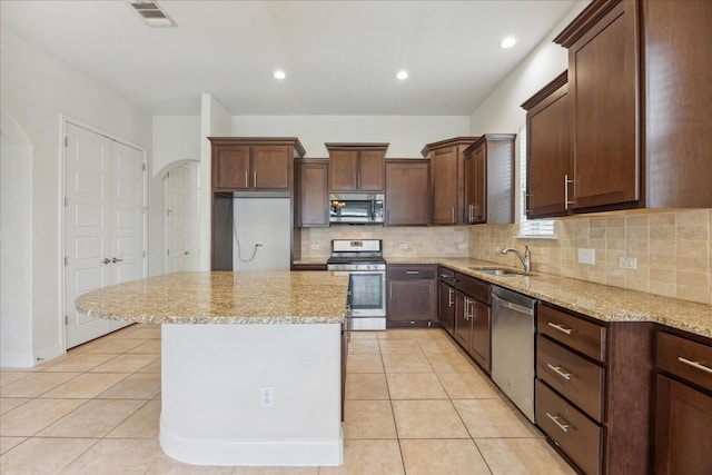 kitchen with tasteful backsplash, light tile patterned floors, a center island, stainless steel appliances, and light stone countertops