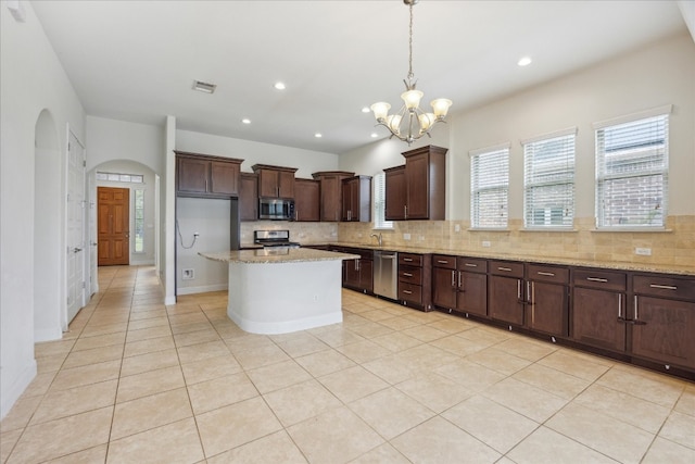 kitchen with a notable chandelier, stainless steel appliances, a center island, light stone countertops, and backsplash