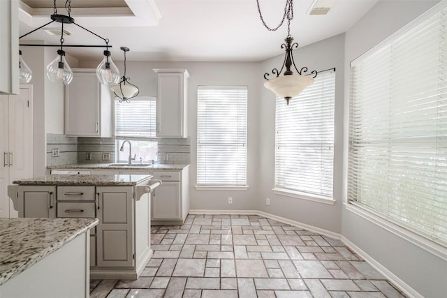 kitchen featuring hanging light fixtures, light stone countertops, sink, and white cabinets