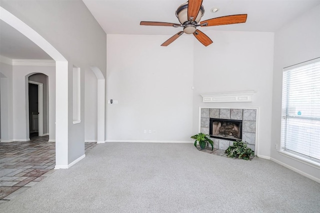 unfurnished living room with a tiled fireplace, ceiling fan, and carpet