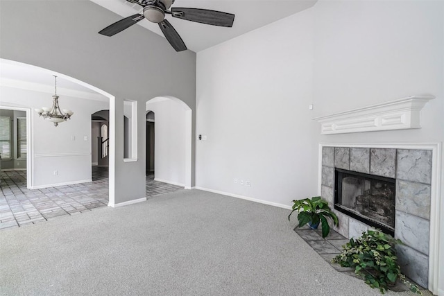 unfurnished living room featuring a tiled fireplace, ceiling fan with notable chandelier, carpet floors, and a high ceiling