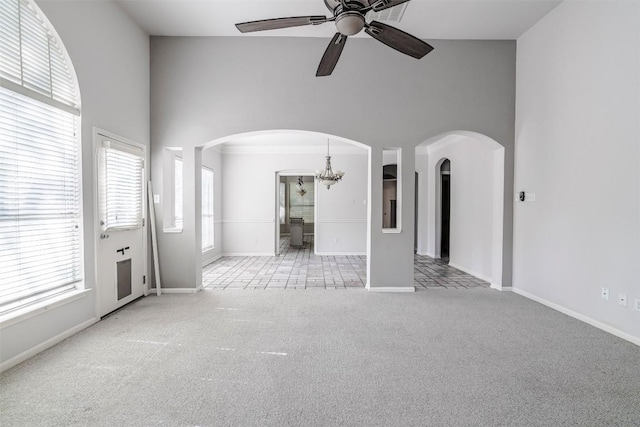 unfurnished living room with a towering ceiling, ceiling fan with notable chandelier, and light carpet