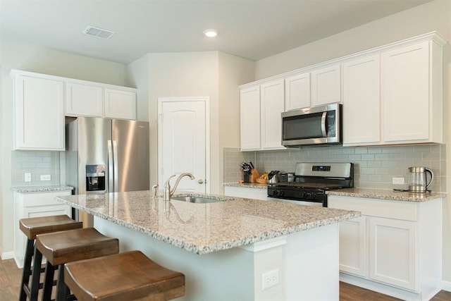 kitchen featuring white cabinetry, sink, stainless steel appliances, light stone countertops, and a center island with sink