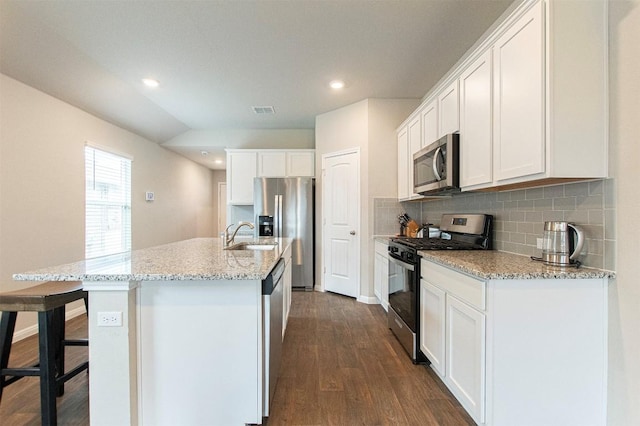 kitchen featuring a kitchen island with sink, light stone countertops, white cabinetry, and stainless steel appliances