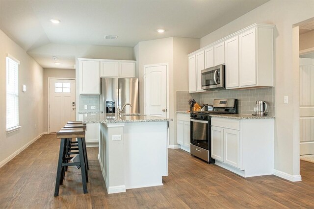 kitchen with wood-type flooring, tasteful backsplash, stainless steel appliances, white cabinets, and an island with sink