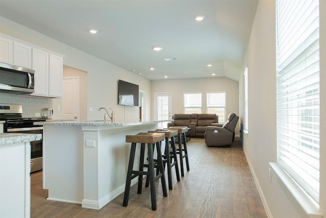 kitchen with a breakfast bar, appliances with stainless steel finishes, tasteful backsplash, an island with sink, and white cabinets