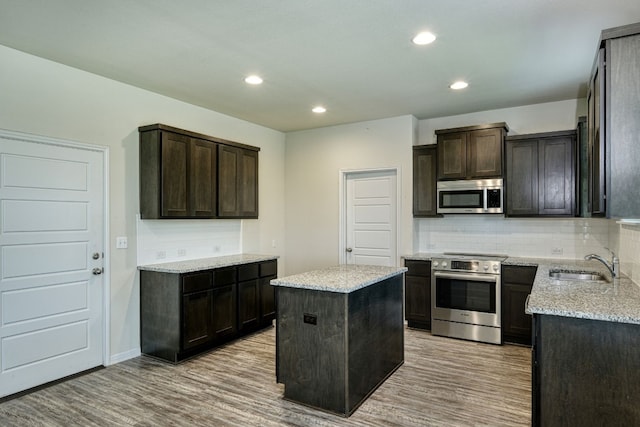 kitchen with light hardwood / wood-style flooring, stainless steel appliances, sink, backsplash, and a center island