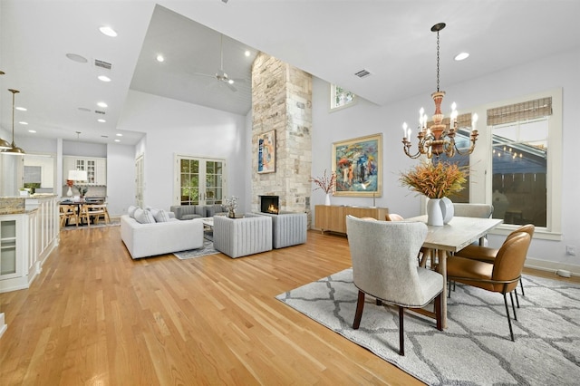 dining room with a stone fireplace, ceiling fan with notable chandelier, light hardwood / wood-style floors, and high vaulted ceiling