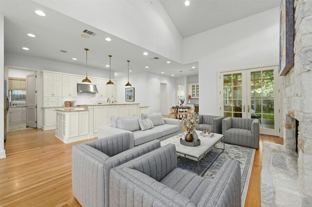 living room with sink, french doors, light hardwood / wood-style flooring, high vaulted ceiling, and a fireplace