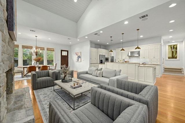 living room with an inviting chandelier, light hardwood / wood-style flooring, and high vaulted ceiling