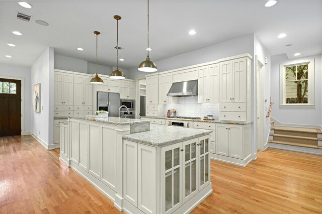 kitchen featuring appliances with stainless steel finishes, light hardwood / wood-style floors, white cabinetry, ventilation hood, and a center island with sink