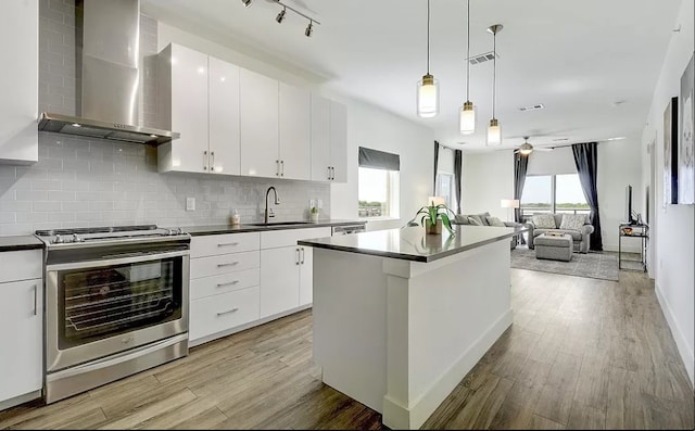 kitchen with appliances with stainless steel finishes, a wealth of natural light, decorative backsplash, and wall chimney range hood