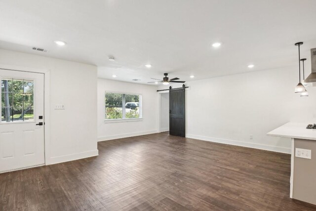 unfurnished living room with ceiling fan, dark hardwood / wood-style flooring, and a barn door