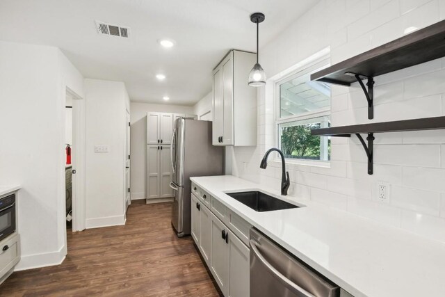 kitchen with appliances with stainless steel finishes, sink, hanging light fixtures, decorative backsplash, and dark wood-type flooring