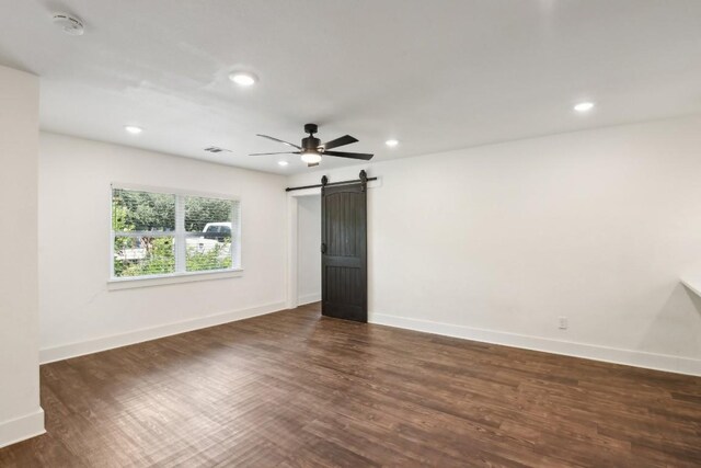 unfurnished room with a barn door, ceiling fan, and dark wood-type flooring