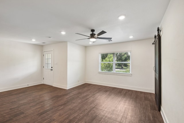 empty room featuring wood-type flooring, a barn door, and ceiling fan