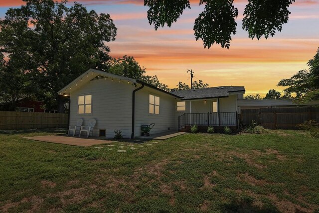 back house at dusk featuring a patio and a yard