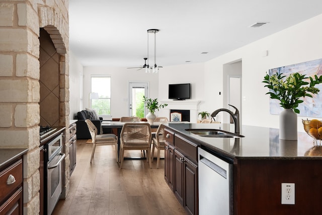 kitchen featuring decorative light fixtures, an island with sink, sink, stainless steel oven, and white dishwasher