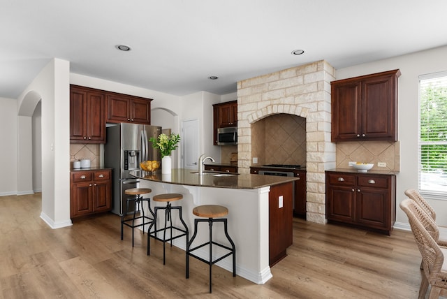 kitchen featuring stainless steel appliances, an island with sink, sink, and light wood-type flooring