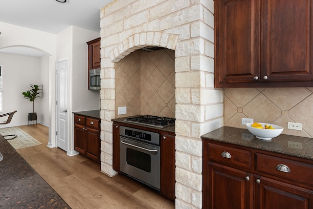 kitchen featuring tasteful backsplash, light hardwood / wood-style floors, dark stone counters, and appliances with stainless steel finishes