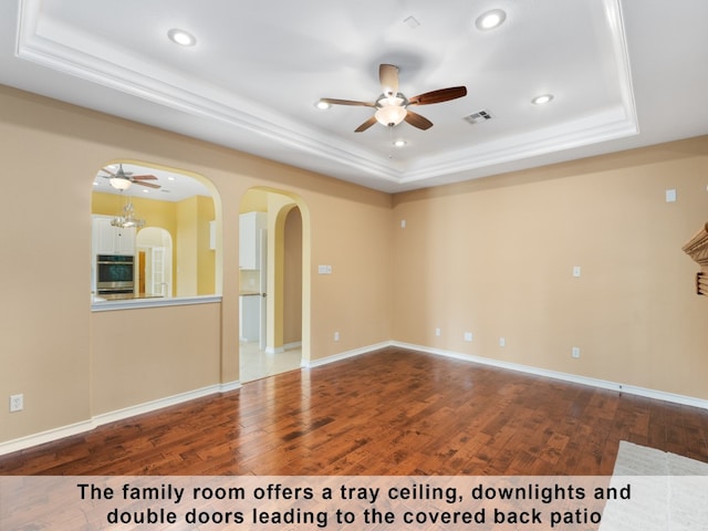 empty room with wood-type flooring, a raised ceiling, and ceiling fan