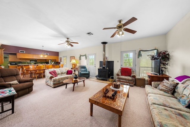 living room with ceiling fan, a wood stove, and light colored carpet