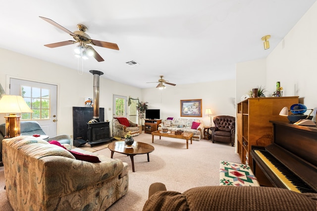 living room with ceiling fan, a wood stove, and light colored carpet