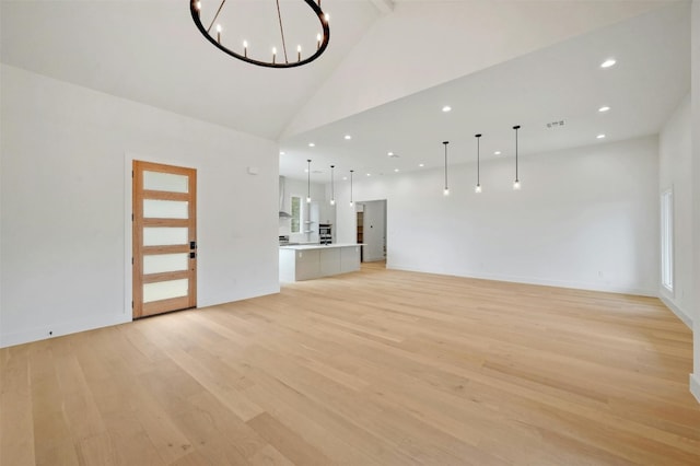 unfurnished living room with high vaulted ceiling, an inviting chandelier, and light wood-type flooring