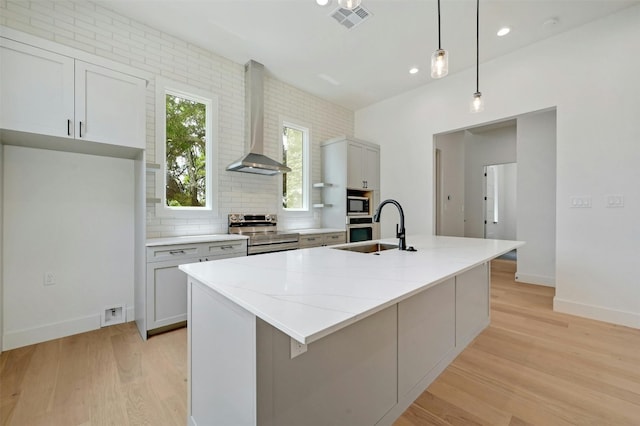 kitchen with light hardwood / wood-style flooring, a center island with sink, wall chimney range hood, stainless steel appliances, and sink