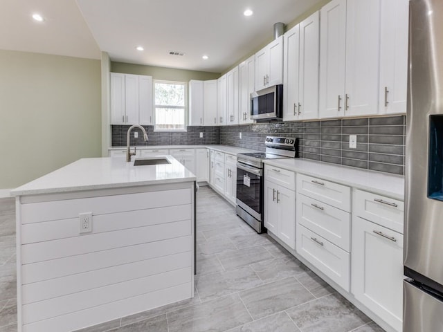 kitchen featuring sink, a kitchen island with sink, white cabinetry, stainless steel appliances, and tasteful backsplash