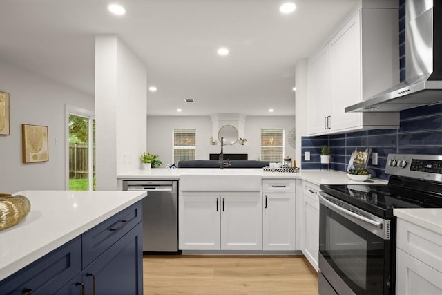 kitchen with appliances with stainless steel finishes, white cabinetry, wall chimney exhaust hood, and sink