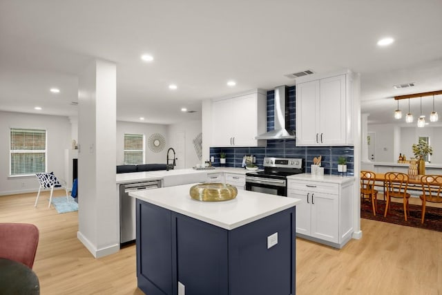 kitchen featuring wall chimney exhaust hood, light hardwood / wood-style floors, kitchen peninsula, and appliances with stainless steel finishes