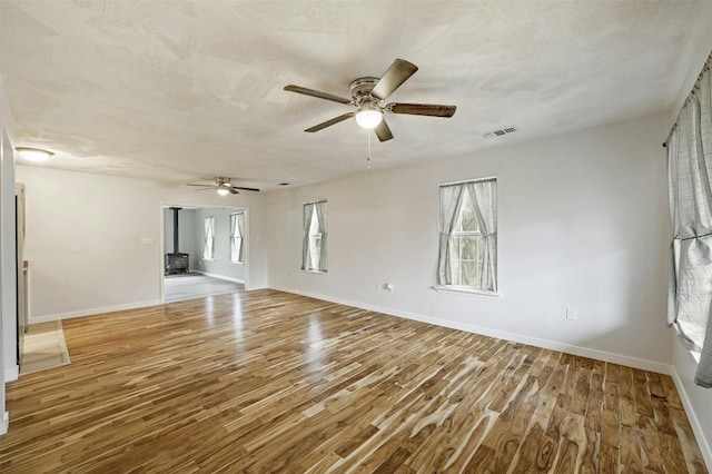 unfurnished room with light hardwood / wood-style floors, a wood stove, a textured ceiling, and ceiling fan