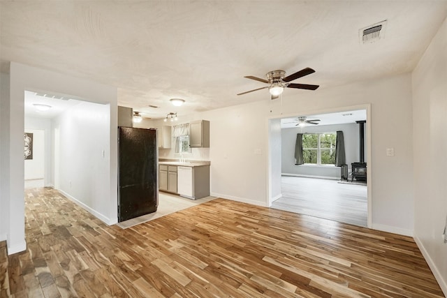 unfurnished living room with a wood stove, light wood-type flooring, and ceiling fan