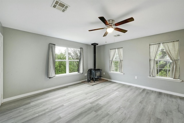 spare room featuring light hardwood / wood-style flooring, a wood stove, plenty of natural light, and ceiling fan