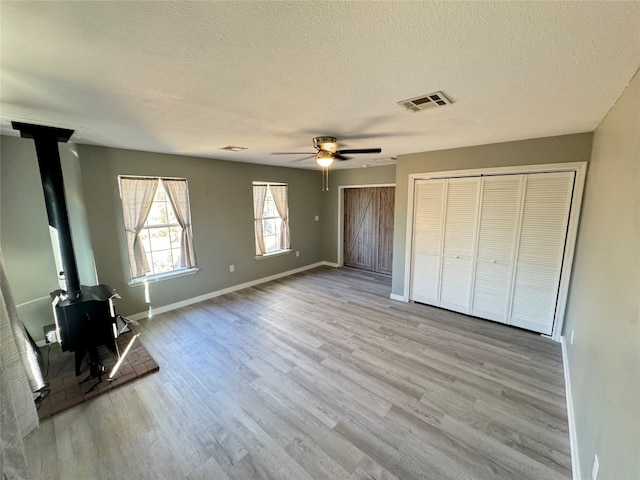 unfurnished bedroom featuring ceiling fan, a textured ceiling, a wood stove, and light hardwood / wood-style flooring