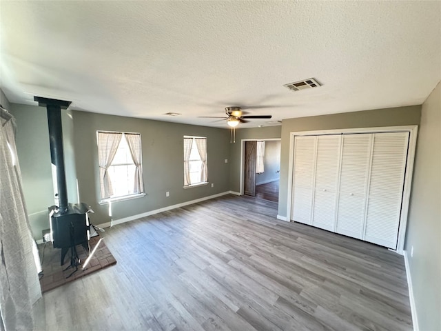 unfurnished living room with a wood stove, a textured ceiling, hardwood / wood-style flooring, and ceiling fan