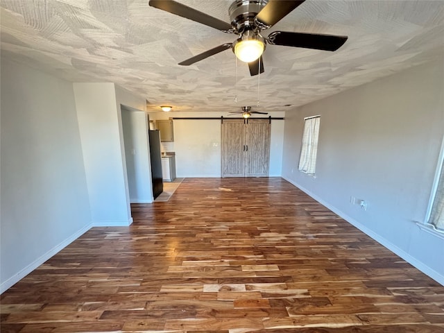 empty room featuring a barn door, dark wood-type flooring, and ceiling fan