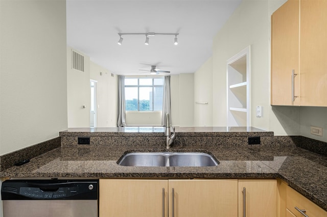 kitchen featuring stainless steel dishwasher, dark stone countertops, sink, and light brown cabinets