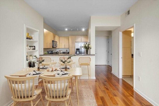 kitchen with built in features, appliances with stainless steel finishes, light brown cabinetry, kitchen peninsula, and light wood-type flooring