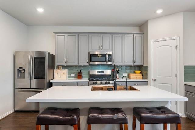 kitchen featuring appliances with stainless steel finishes, dark hardwood / wood-style floors, gray cabinets, and an island with sink