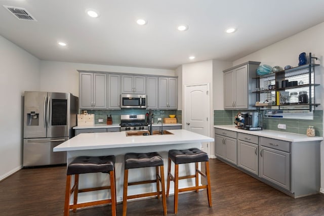 kitchen with tasteful backsplash, a center island with sink, dark hardwood / wood-style floors, and stainless steel appliances