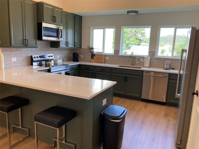 kitchen featuring stainless steel appliances, light wood-type flooring, sink, kitchen peninsula, and backsplash